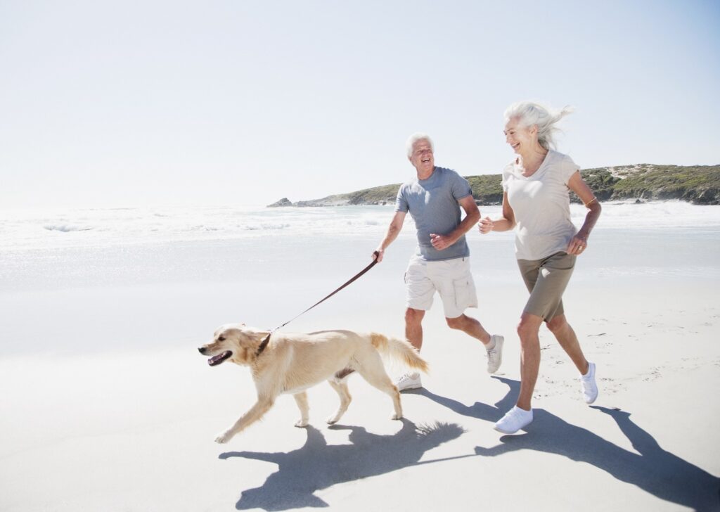 Active over-50 couple walking their dog on the beach symbolizes vitality, balance, and strong bone health through mobility.